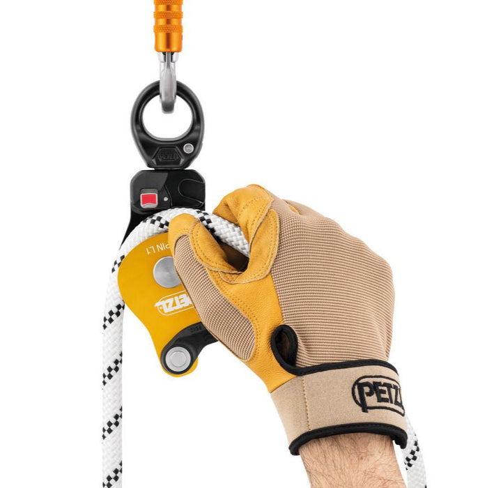 Hand model wearing gloves installing a rope on the Petzl Spin L1 Pulley while it is connected to the anchor