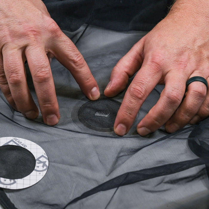 Model applying Gear Aid Tenacious Tape Mesh Patch to repair a bug screen 